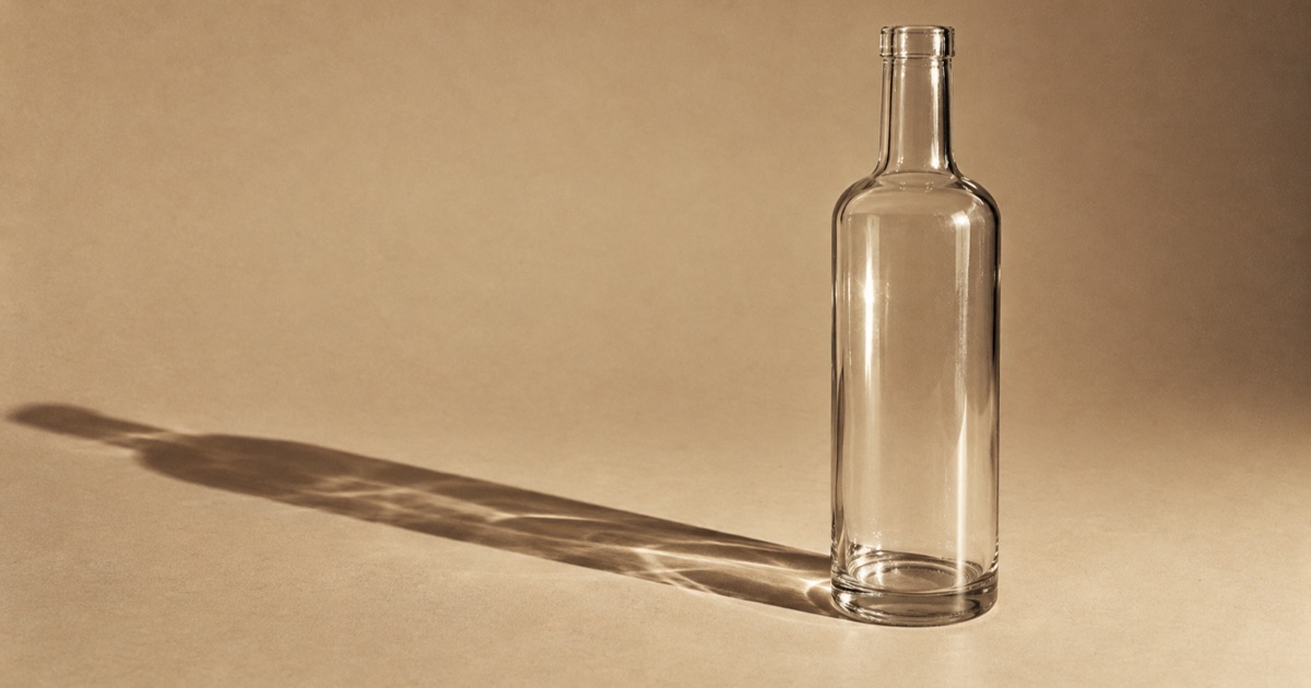 Bouteille en verre transparent sans étiquette posée sur un fond uni, avec une ombre portée nette